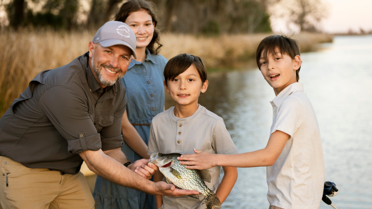 A family of four on the river showing their catch after a day of fishing.