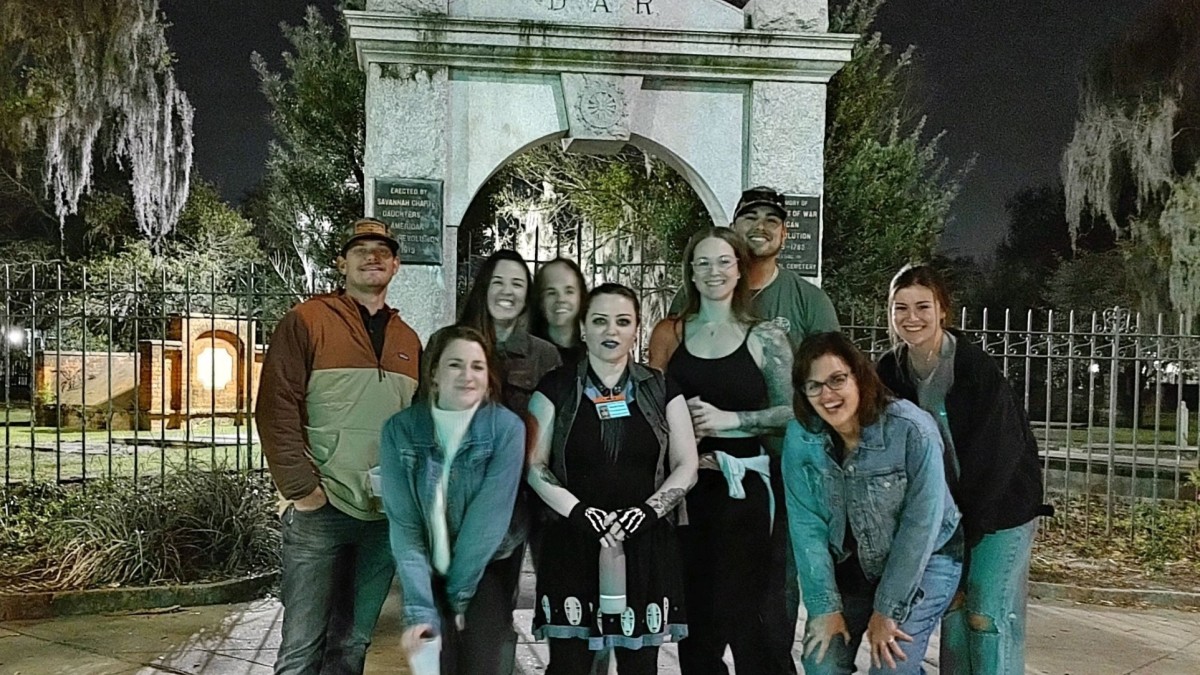 A group of people on a ghost tour in front of a cemetery.