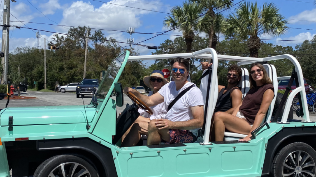 A group of people in a mint green colored Mini Moke vehicle.