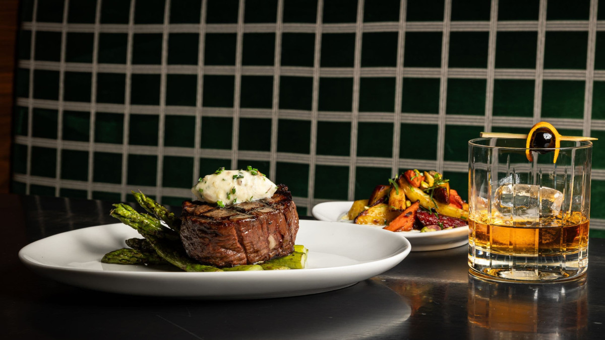 Filet mignon on a bed of asparagus topped with butter served on a white plate.