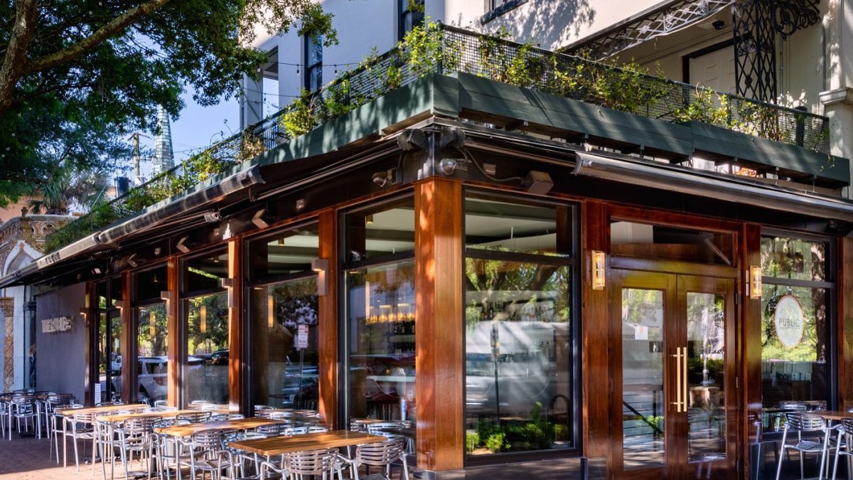 The exterior view of a corner restaurant in downtown Savannah with outdoor seating, including a rooftop.