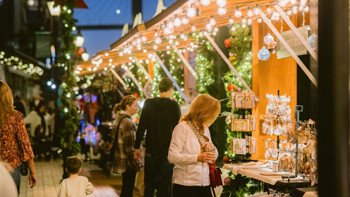 Shoppers browse festive stalls decorated with wreaths, ornaments, and twinkling lights at the Savannah Christmas Market in Plant Riverside District.