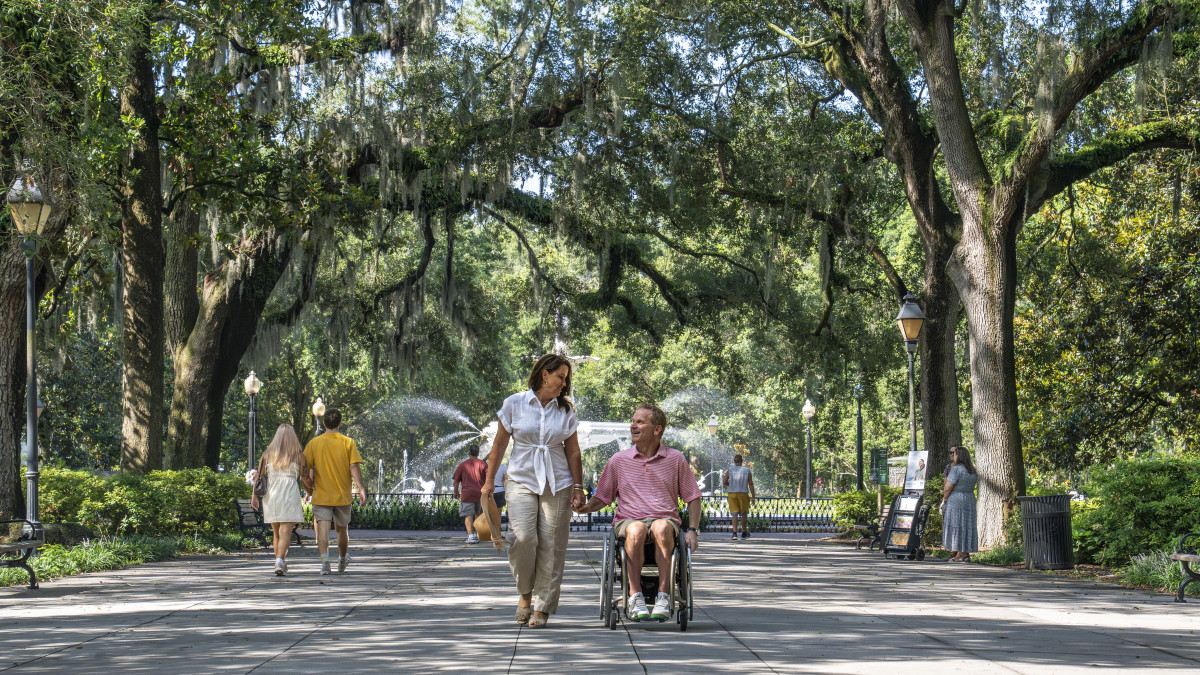 a couple walking in Forsyth Park, man in wheelchair, sunny day.