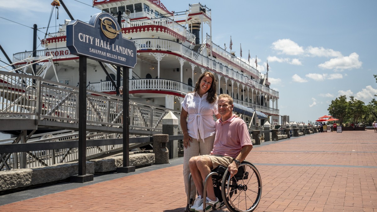 couple on river street in front of riverboat, man in wheelchair