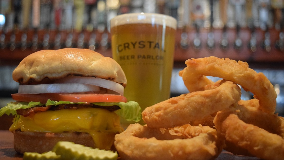Crystal Beer Parlor’s loaded burger with a side of golden onion rings and a beer are pictured.