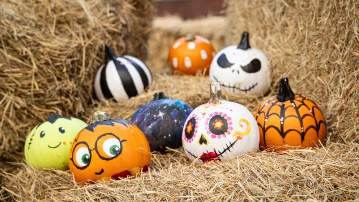 Several pumpkins painted as cheerful jack-o’-lanterns rest on top of stacked hay bales, creating a playful fall display.