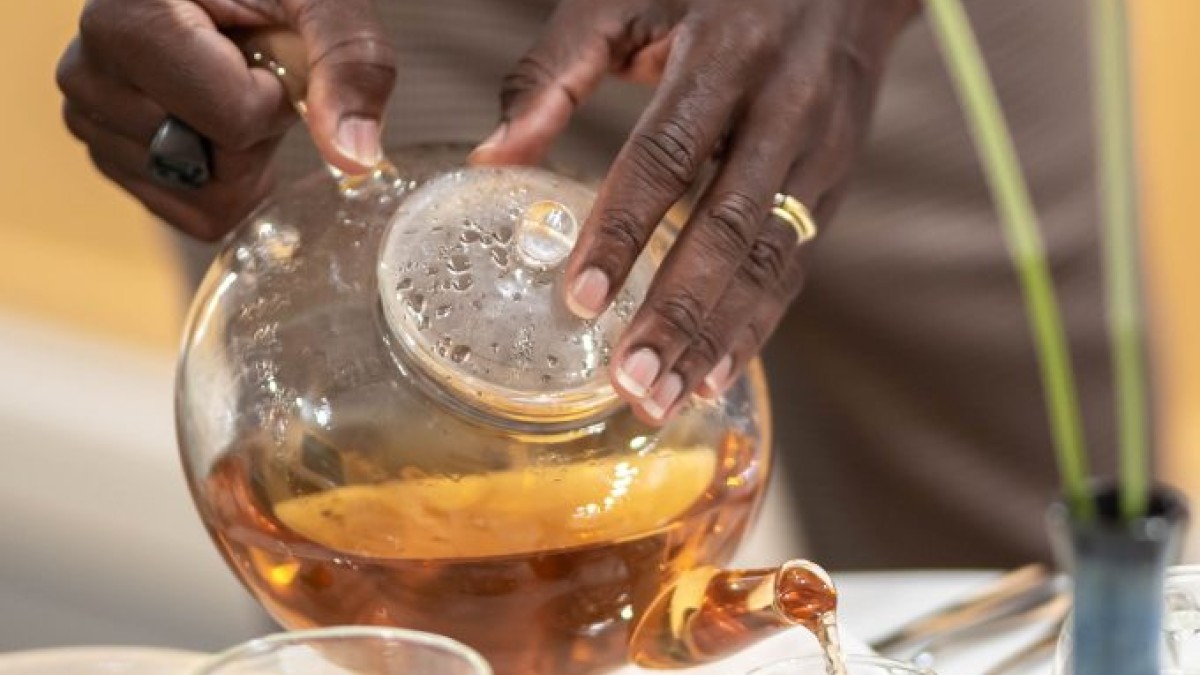 African American hands seen pouring tea from a glass teapot.