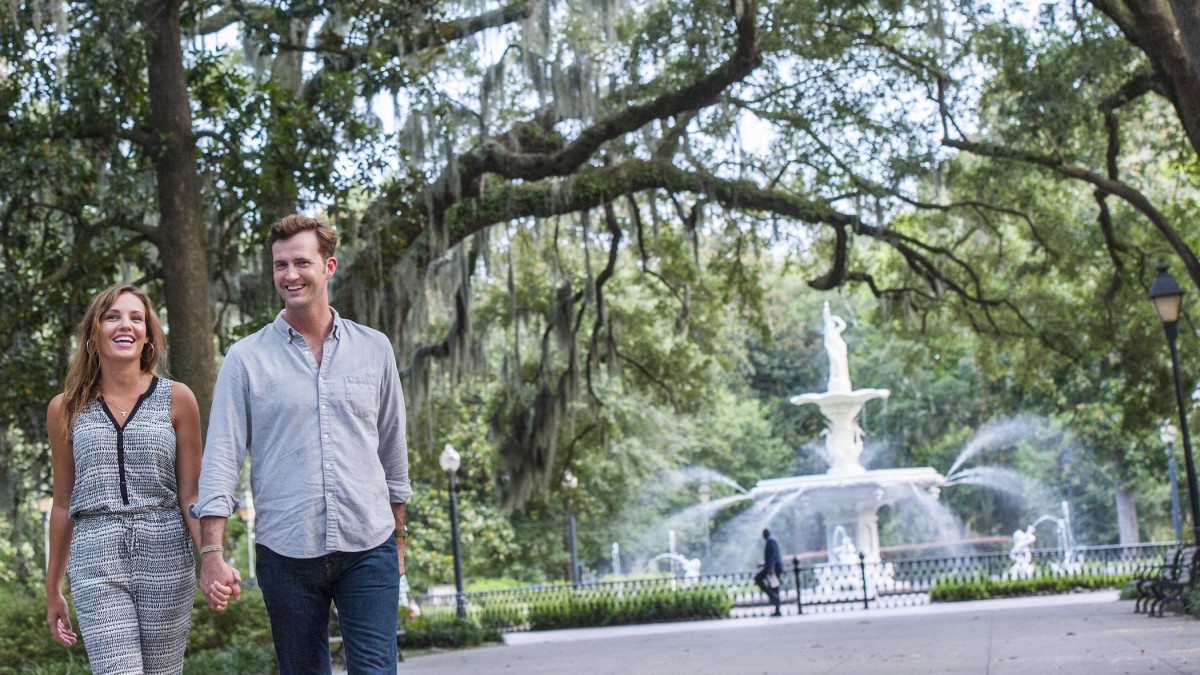 A couple walking through Forsyth Park with the fountain in the background.