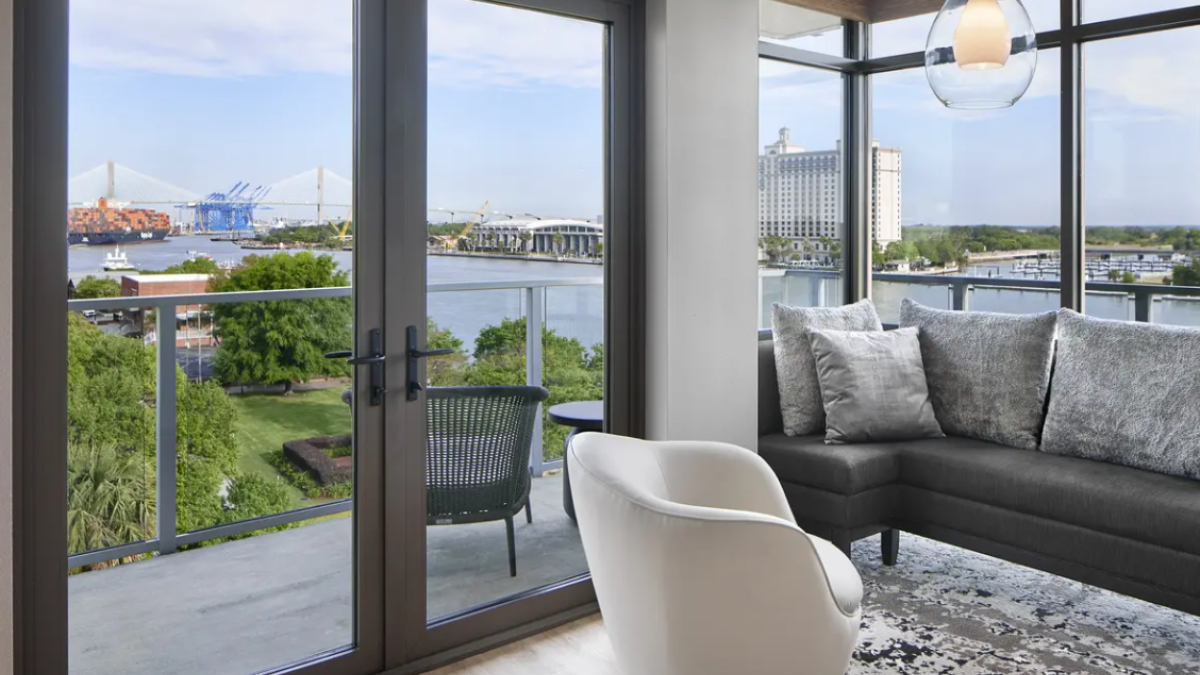 Modern guest suite at AC Hotel Savannah featuring floor-to-ceiling glass doors, a private balcony and sweeping views of the Savannah River.
