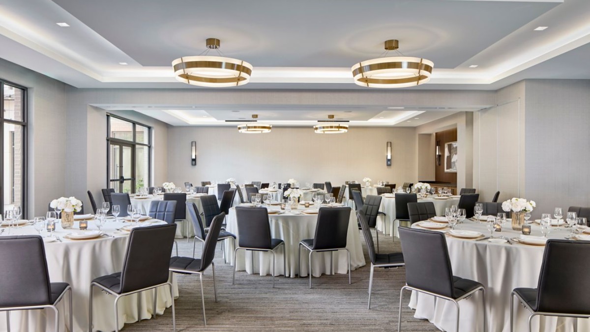 Bright, modern ballroom at AC Hotel Savannah set for a wedding reception, featuring round tables with white linens, soft neutral décor, contemporary lighting and an open, elegant layout.