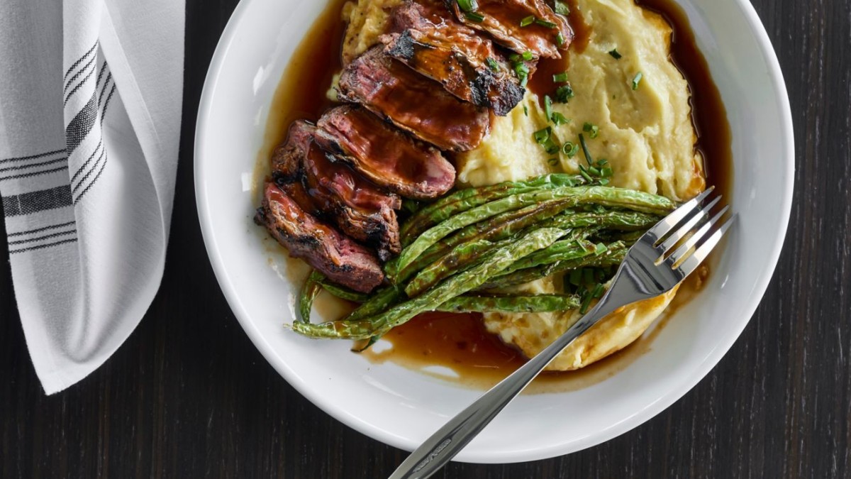 Grilled romesco steak served at Lavender Rooftop Kitchen & Bar at AC Hotel Savannah, plated with creamy mashed potatoes, roasted asparagus and a rich pan sauce.