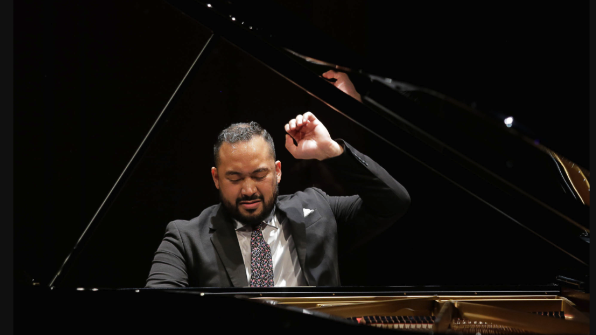 Pianist Johnathan Mamora is sitting at the piano performing a selection.