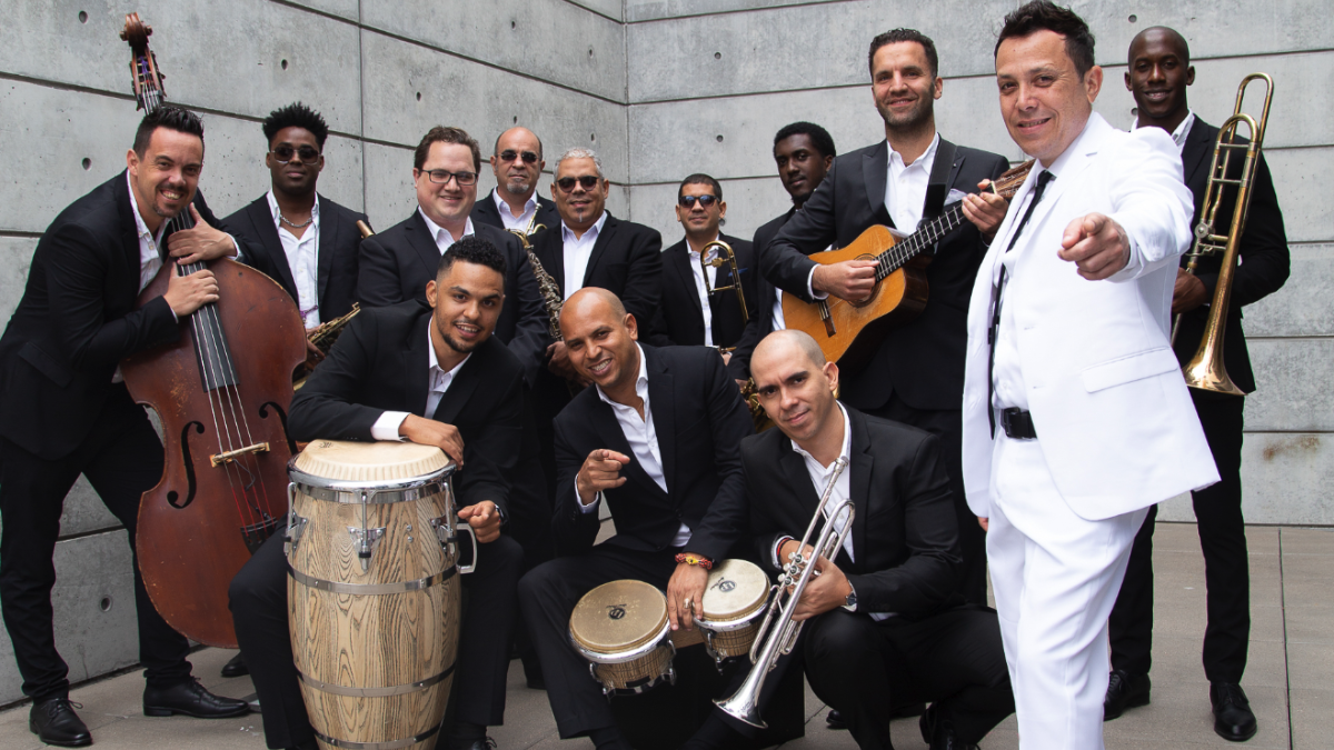 Members of a Latin jazz ensemble pose with brass instruments, percussion and string bass during a Savannah Music Festival 2026 “Havana Nights” promotional shoot.