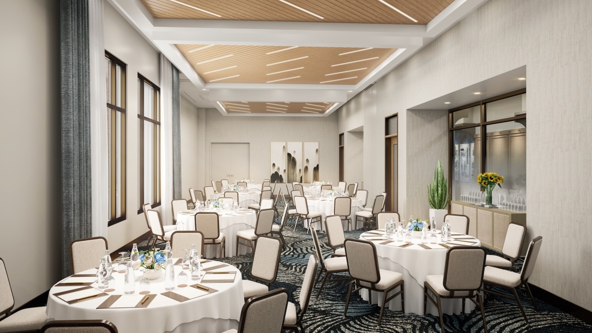Meeting and event space at Tempo by Hilton Savannah Historic District, set with round banquet tables, neutral décor, upholstered chairs, and a modern ceiling with warm wood accents and soft lighting.