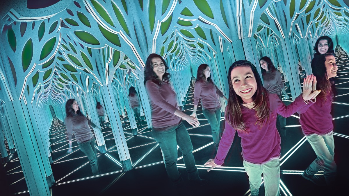 Girl exploring a mirrored light tunnel exhibit with geometric LED flooring and tree-shaped panels.