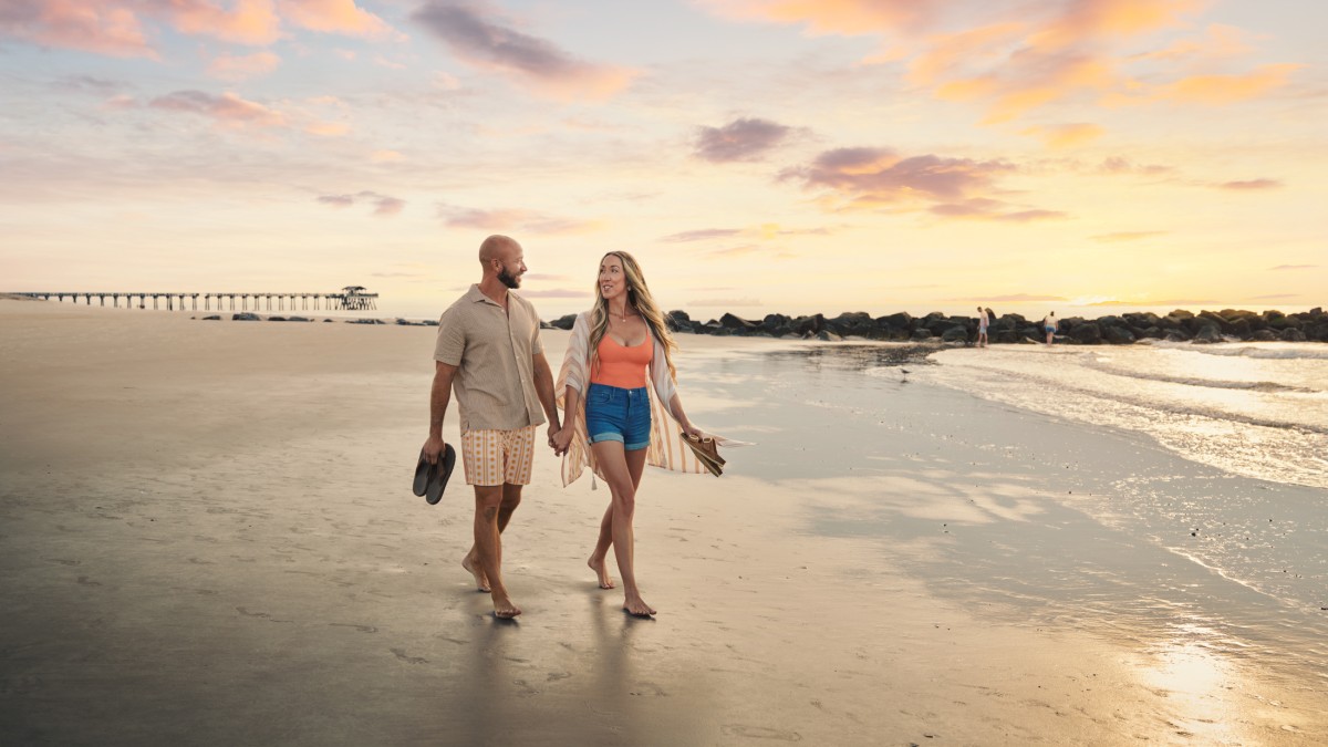 Couple holding hands while walking along Tybee Island beach at sunset.