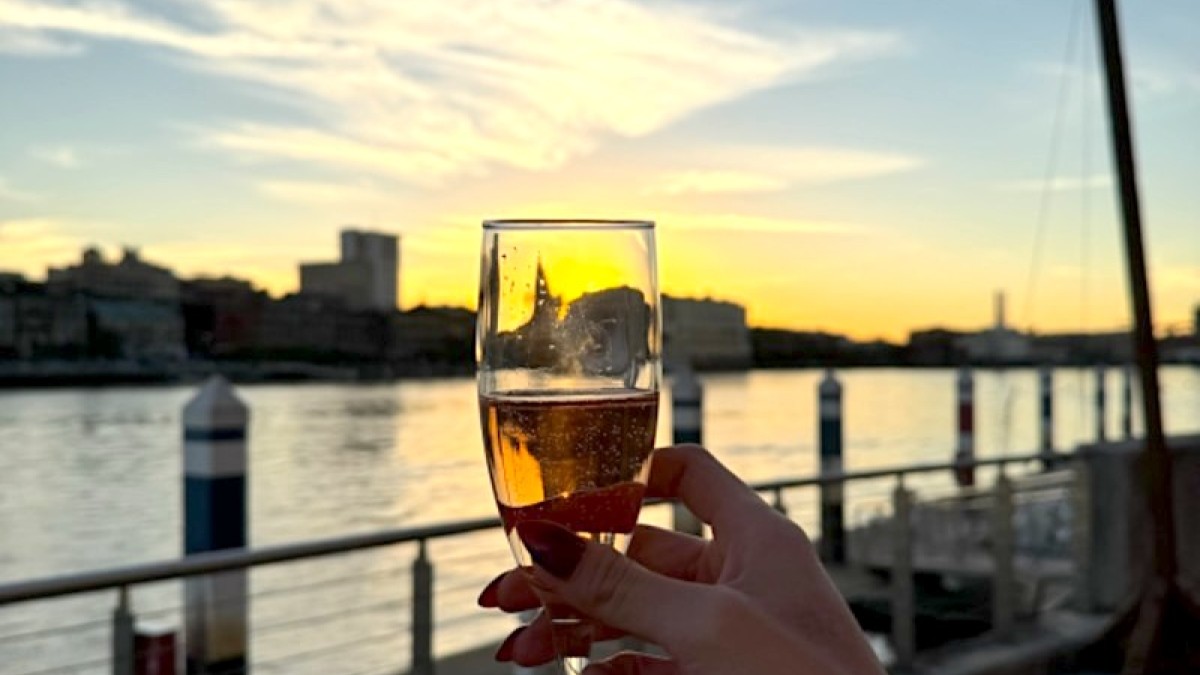 The hand of a woman holding a wine glass outside at sunset.