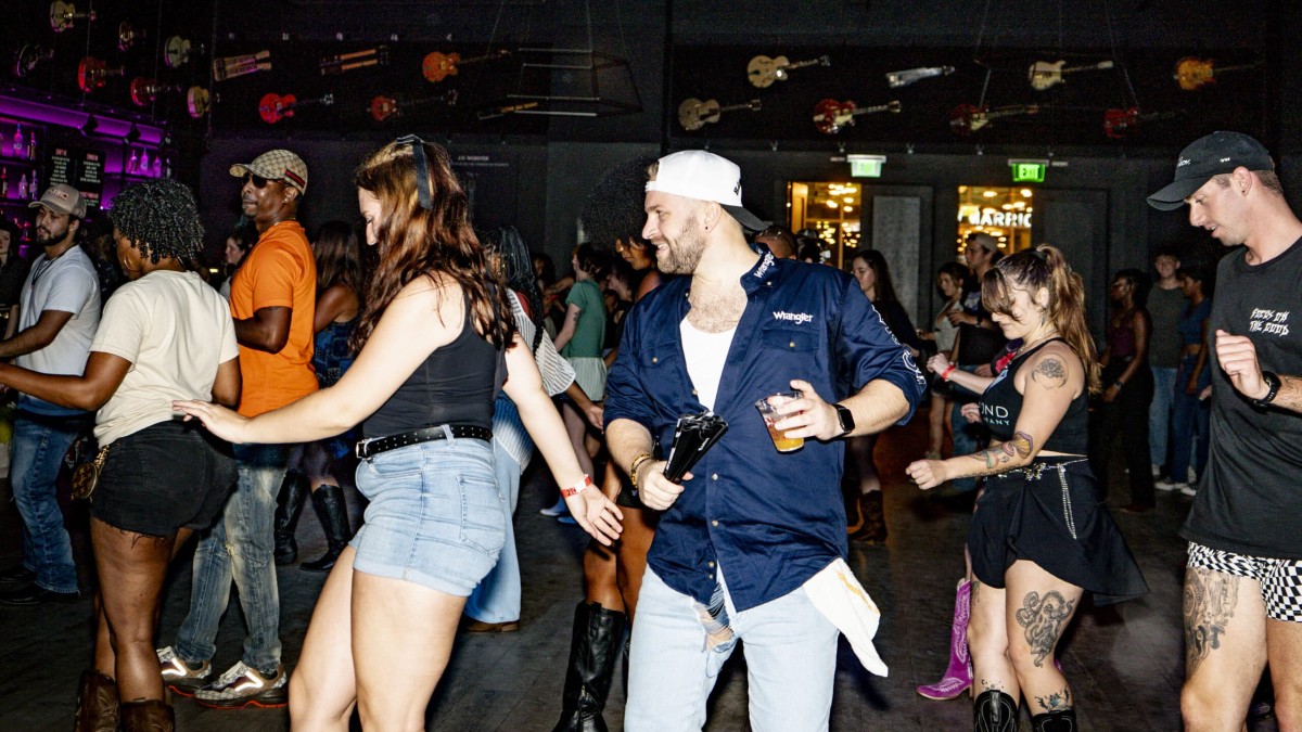 Numerous people, dressed casually while line dancing on the dance floor.