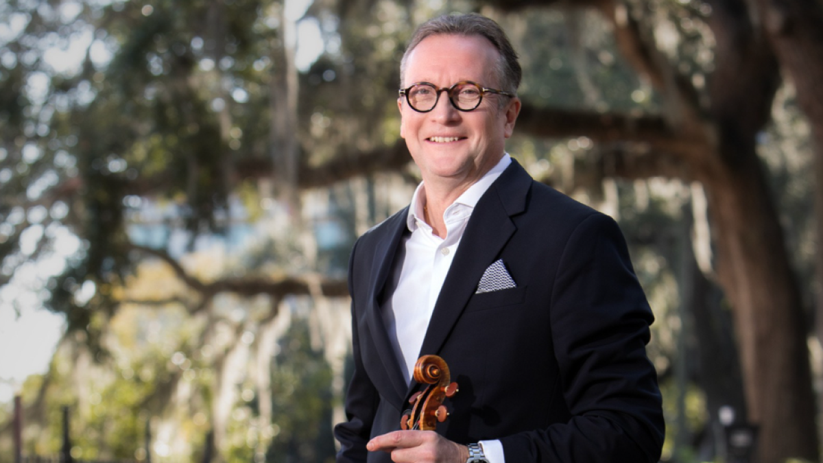 Man holding violin outdoors under oak trees for Savannah Philharmonic Orchestra performance in Savannah, GA.