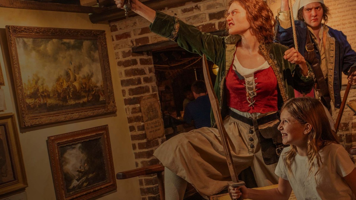 Actors in pirate costumes perform inside Savannah’s Pirates and Treasure Museum while a child smiles and holds a sword.