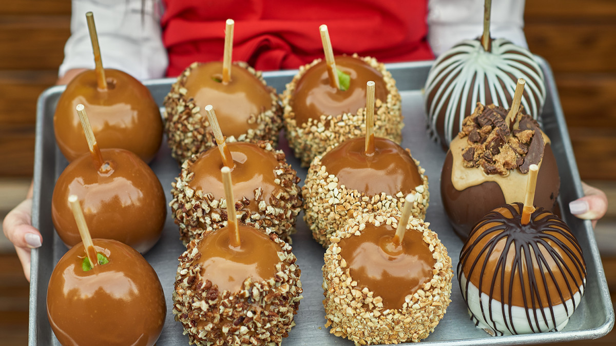 Tray of assorted caramel apples with nuts and chocolate toppings.