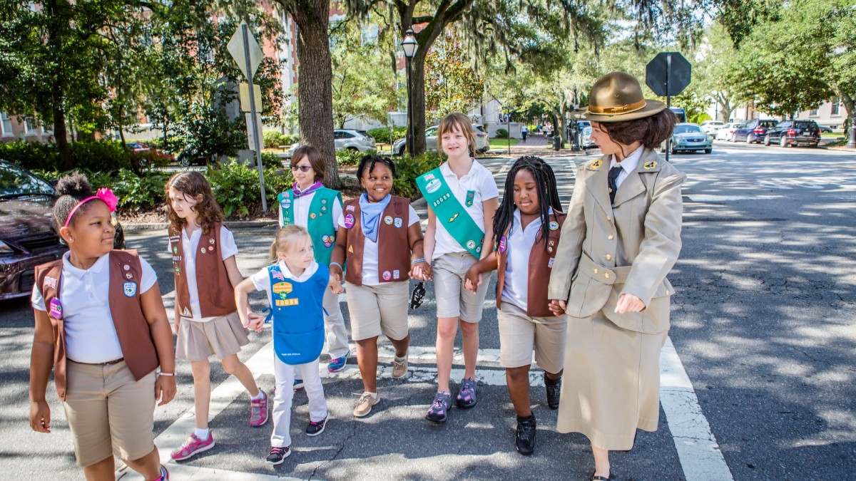 Girl Scouts in uniform cross a street in Savannah with a guide dressed as Juliette Gordon Low.