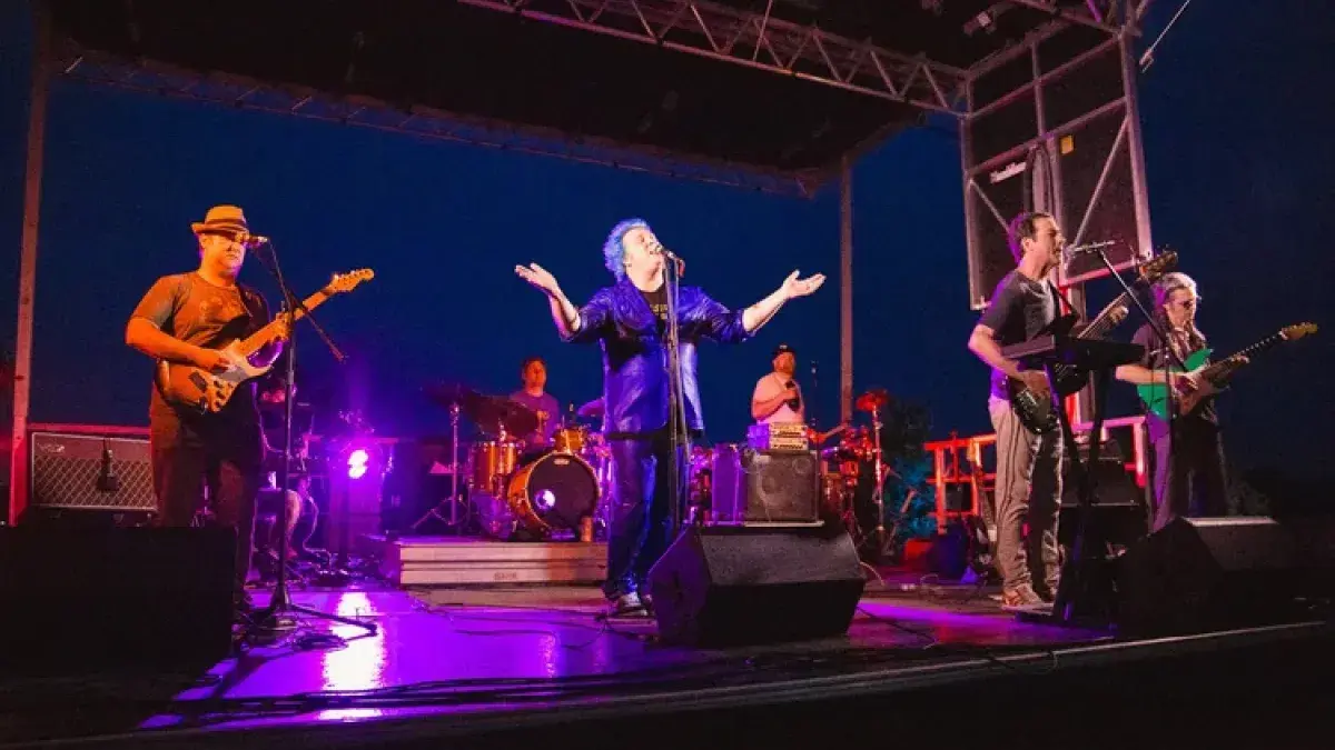 A live band performs on an outdoor stage at night, with colorful lighting and musicians playing instruments.