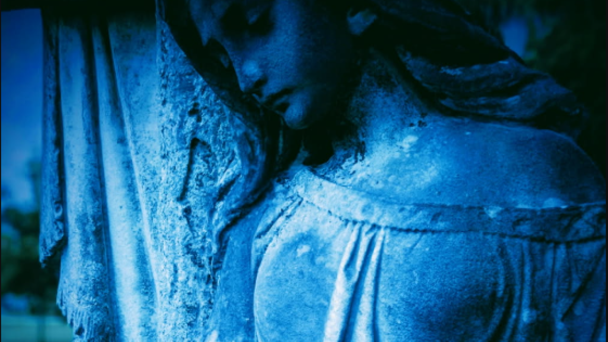 Blue-toned statue in a Savannah cemetery illuminated in eerie light.
