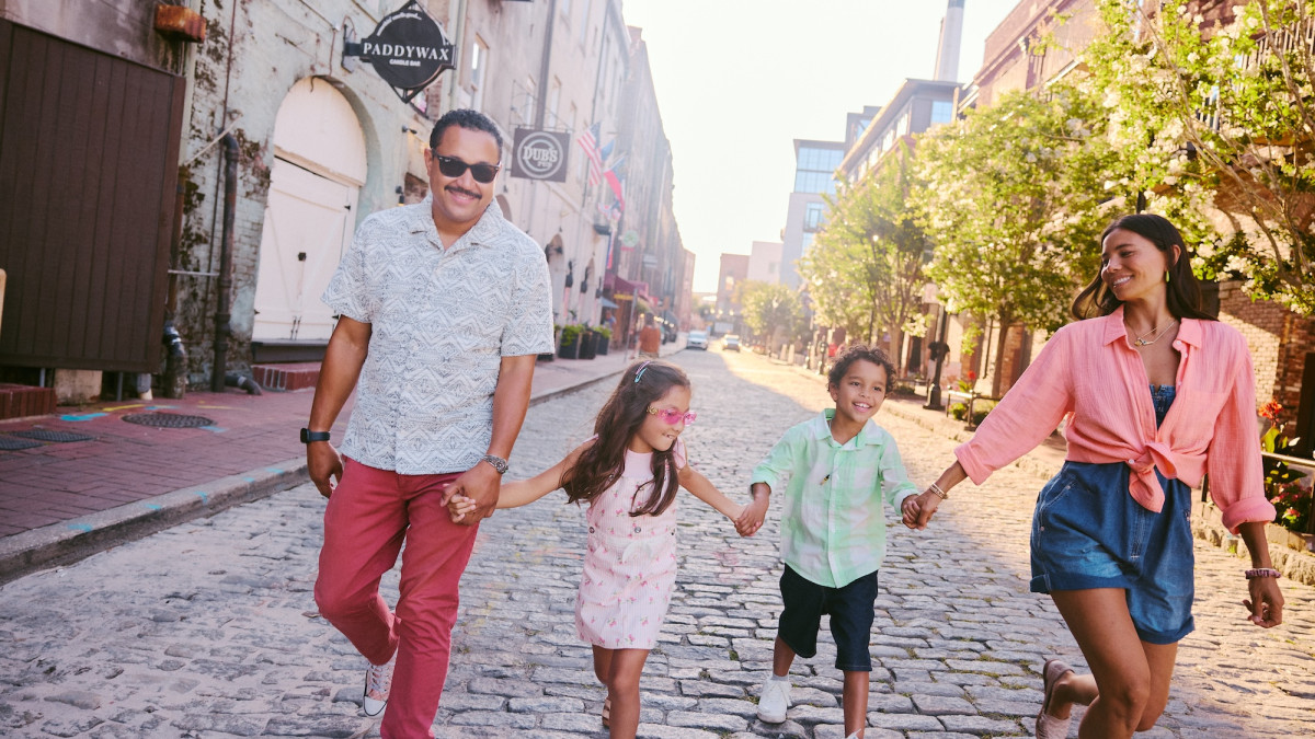 A family of four walks hand in hand along the cobblestones of River Street in Savannah.