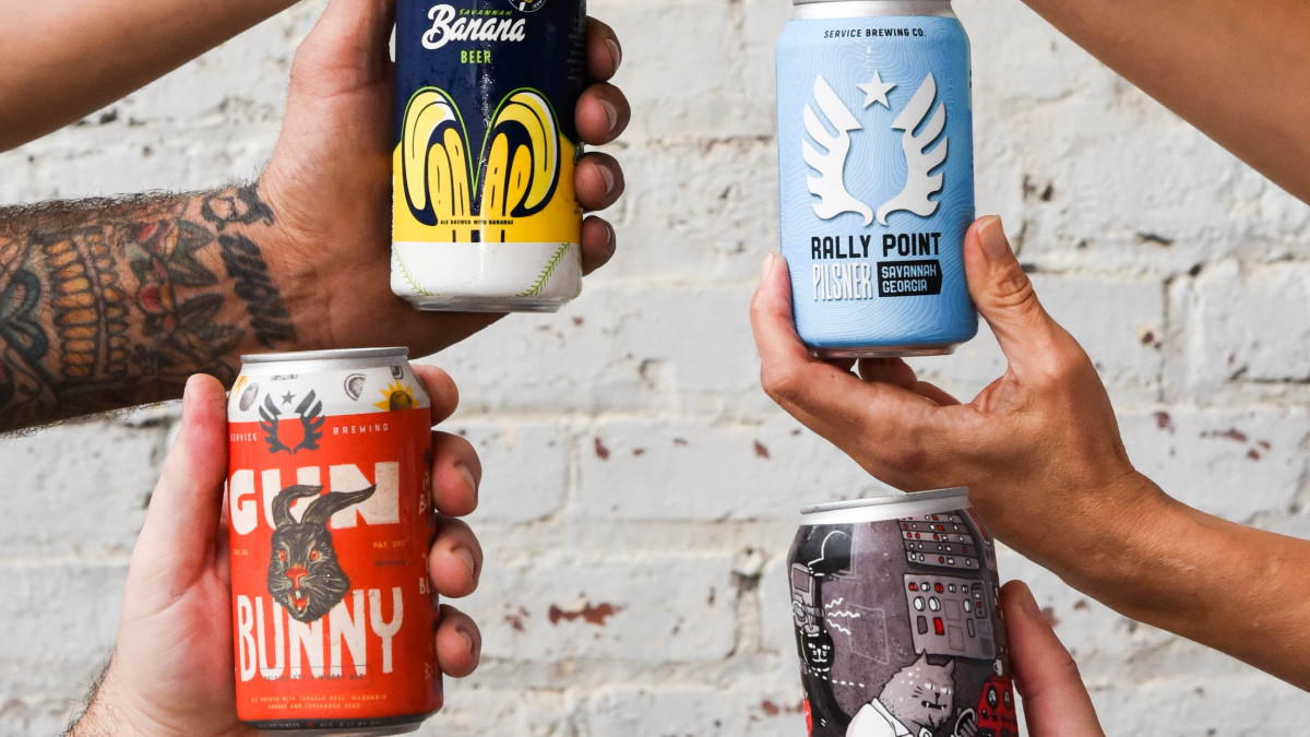 Hands of multiple people holding Service Brewing beer cans.