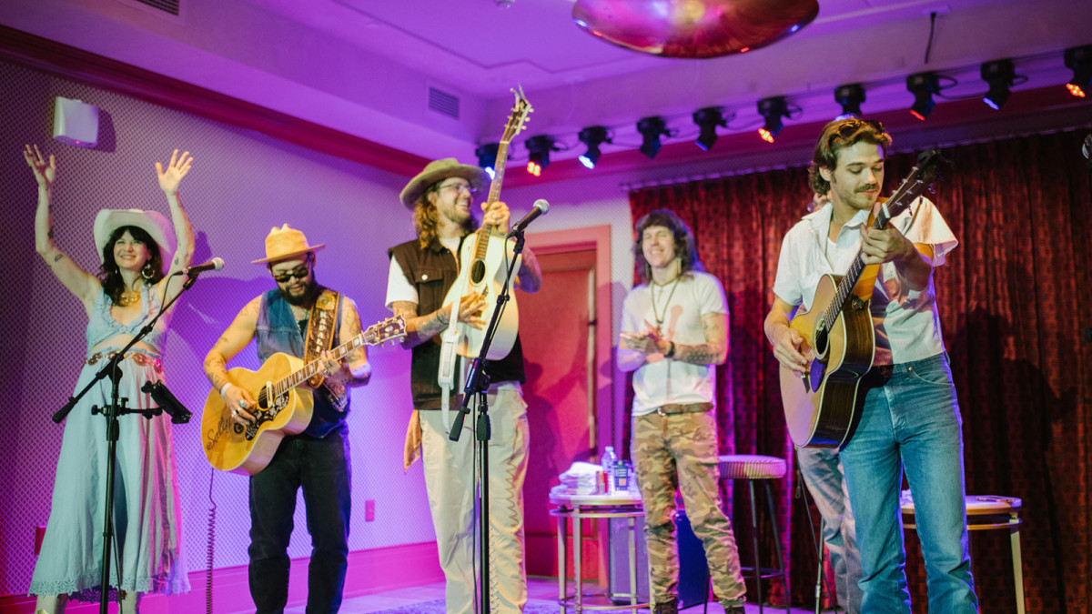 Five musicians perform with acoustic guitars and microphones under vibrant purple and pink stage lighting at Nickel & Oak Lounge in Savannah.