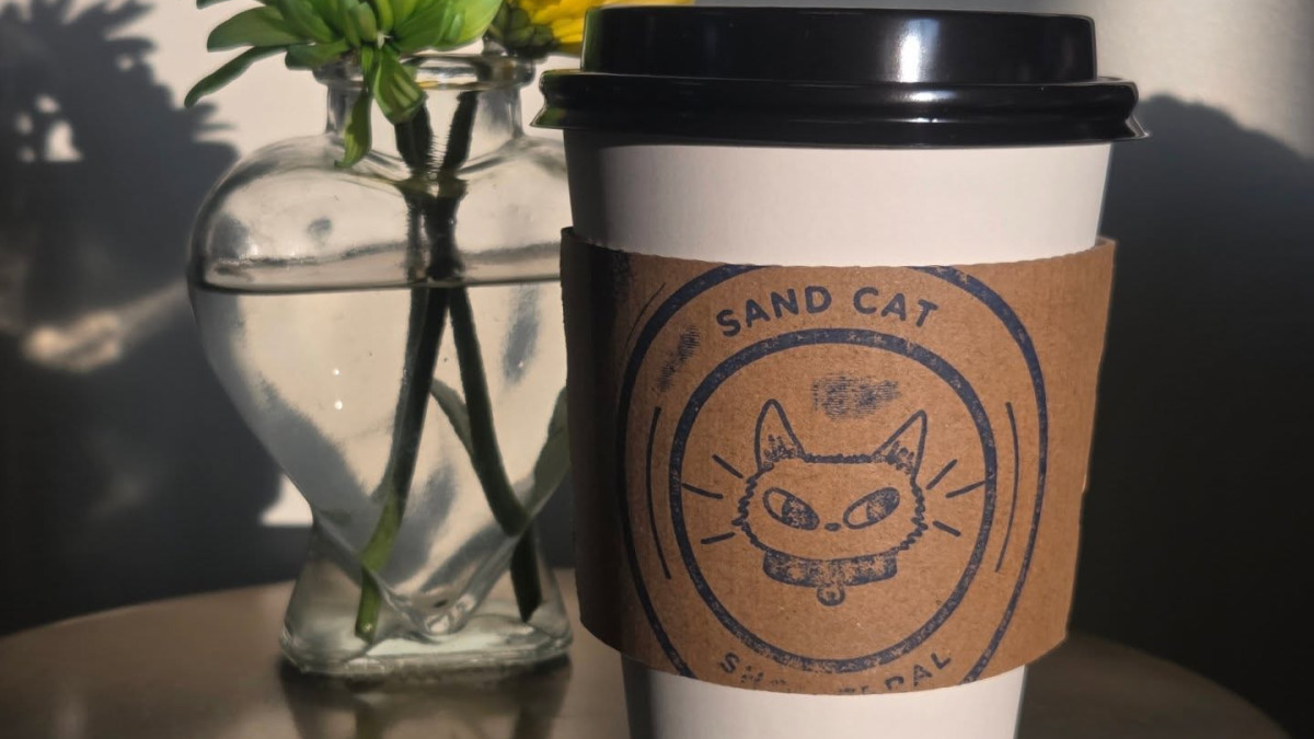 A to-go coffee cup and small glass vase with a flower sitting on a round table.