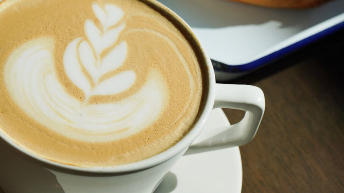 Close-up of a freshly brewed latte with intricate leaf-shaped foam art, served alongside a golden, flaky pastry and a small cup of coffee at Stevedore Bakery in Savannah.