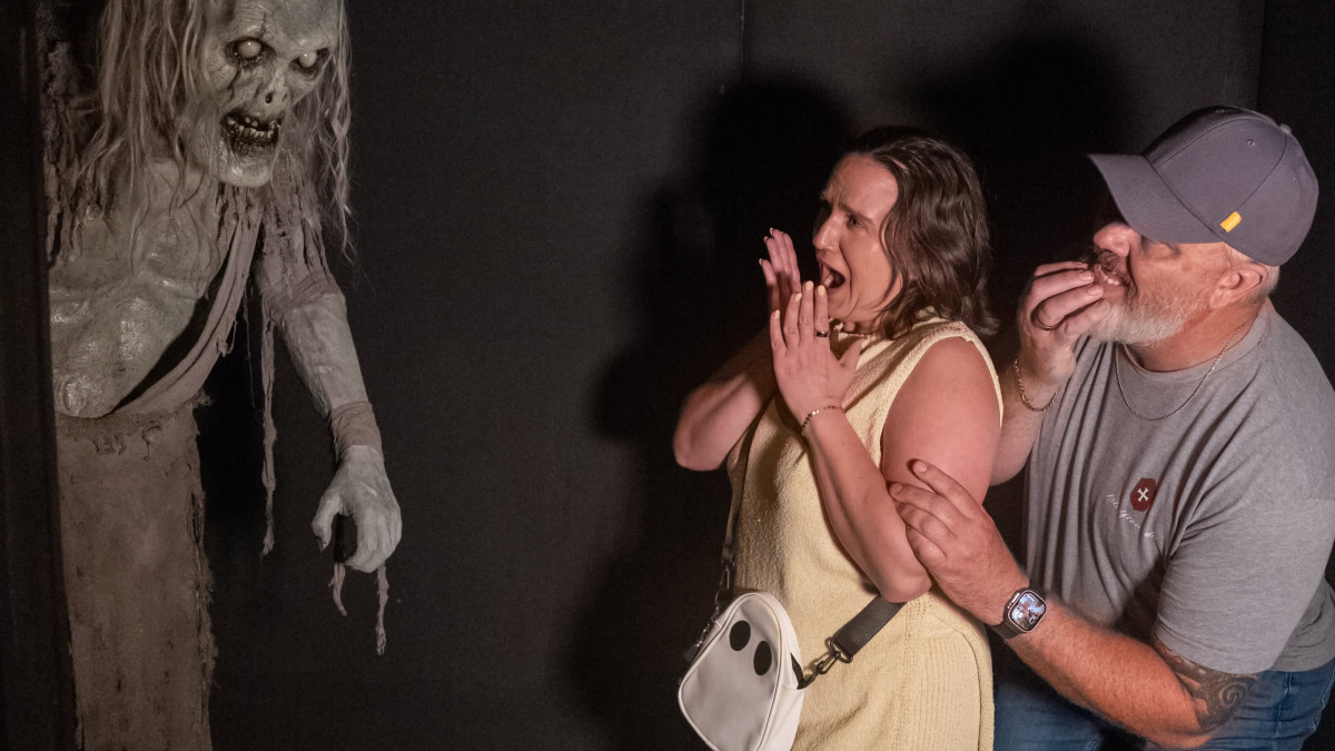 Two startled visitors recoil from a terrifying, gray-skinned figure with glowing eyes inside The Haunted Savannah haunted house attraction.