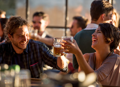A man and a woman cheering with drinks in a lively restaurant.