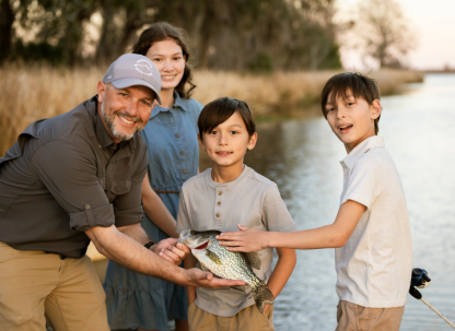 A family of four on the river showing their catch after a day of fishing.