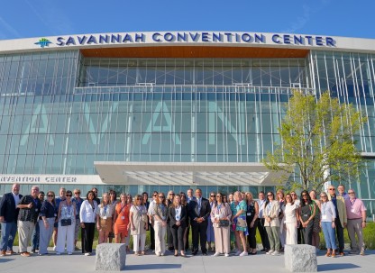 A large group posing for a photo at the front entrance of the Savannah Convention Center.