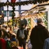 Crowds gather under garlands and twinkling lights at the Savannah Christmas Market at Plant Riverside District, exploring festive vendor stalls decorated for the holidays.
