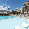 Outdoor pool deck at The DeSoto Savannah featuring a shallow sun shelf with in-water lounge chairs, palm trees, poolside seating and views of the hotel's rooftop terrace beneath a bright blue sky.
