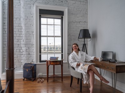 A young woman lounging in a chair in a hotel room wearing a white bathrobe.