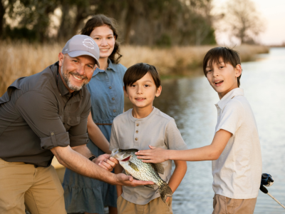 A family of four on the river showing their catch after a day of fishing.