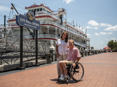 couple on river street in front of riverboat, man in wheelchair