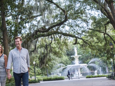 A couple walking through Forsyth Park with the fountain in the background.