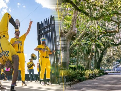 Savannah Bananas players in yellow uniforms dance and perform acrobatics outside Grayson Stadium, alongside a serene tree-lined path leading to the iconic Forsyth Park fountain in Savannah, Georgia.